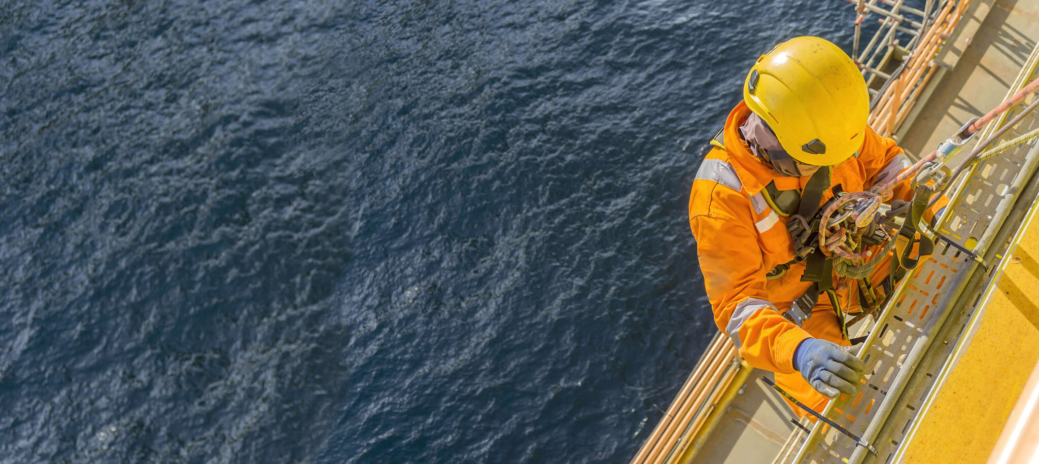 Industrial worker in orange safety gear and yellow helmet working at height over water